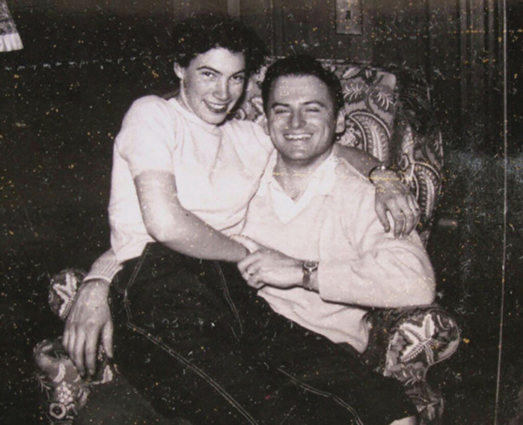 A black and white vintage photo of Bert Berkley and Joan Berkely as young adults. She is sitting on his lap and they are both smiling.